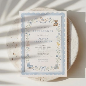 May include: Baby shower invitation with a light blue scalloped border and floral accents. The invitation includes the text "Join us for a Baby Shower" and details for Olivia Alexander's baby shower, including the date, time, and location.