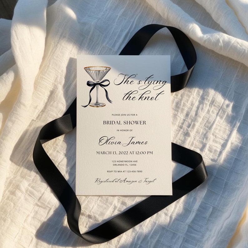 May include: A white bridal shower invitation with black calligraphy that reads "She's tying the knot". The invitation features a watercolor illustration of a martini glass with a black ribbon and bow. The invitation includes the bride's name, the date and time of the shower, the address, and RSVP information.