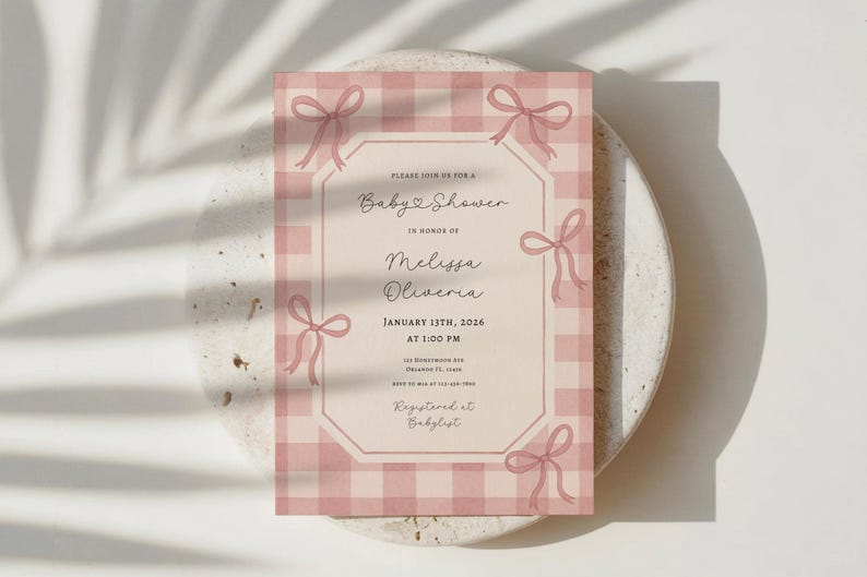 May include: A baby shower invitation with a pink gingham pattern and decorative bows. The invitation includes the text "Baby Shower" and details for Melissa Oliveria's baby shower on January 13th, 2026.