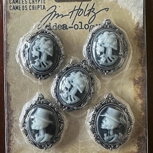 May include: Five oval-shaped crypt cameos with silver-colored frames. Each cameo features a white relief design against a black background. The package includes text that reads "CRYPT CAMEOS" and "5 PIECES".