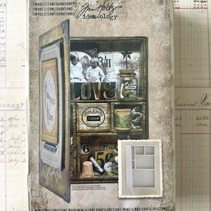 May include: A Tim Holtz Idea-ology Mini Configurations Book packaging box featuring a hinged door and multiple interior compartments. The box displays a decorative collage of vintage-style items including a glass jar, thread spools, and text labels.