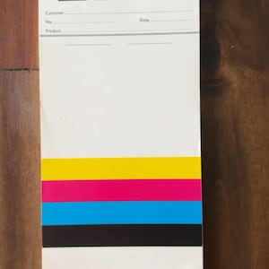 May include: A white rectangular notepad featuring the BASF logo and the text BASF Wyandotte Corporation Pigments Division at the top. Below are lines for Customer, No., Date, and Product. The bottom section displays horizontal yellow, magenta, cyan, and black bars.