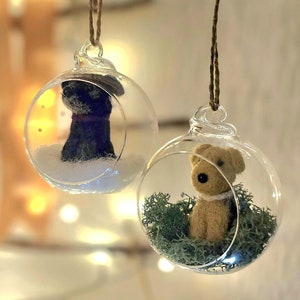 May include: Two glass ornaments with a small dog figurine inside each. One ornament has a black dog figurine in a snowy scene. The other ornament has a brown dog figurine in a bed of green moss.