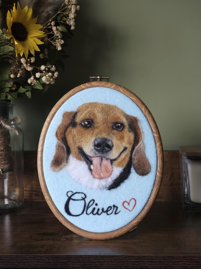 Puede incluir: Retrato ovalado enmarcado de un perro con pelaje marr&oacute;n y canela, una lengua rosada y el nombre "Oliver" en cursiva. El fondo es azul claro y el marco es de madera. Un coraz&oacute;n rojo est&aacute; al lado del nombre.