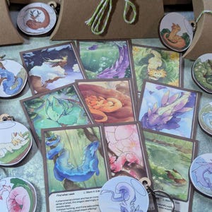 Peut inclure: Un assortiment de porte-clés et de cartes sur le thème de la fantaisie, avec des illustrations de dragons colorés. Les porte-clés sont ronds avec des anneaux argentés, et les cartes présentent des scènes de dragons variées.