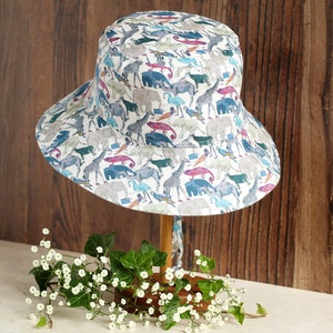 May include: A white sun hat with a colorful animal print design. The hat has a wide brim and a chin strap.
