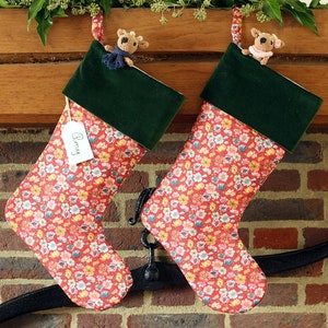 May include: Two red and white floral Christmas stockings with green velvet cuffs. The stockings are hung on a fireplace mantel with a black metal hook. One stocking has a name tag that says "Benny".