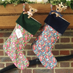 May include: Two Christmas stockings with floral patterns, one green with a pink reindeer and the other blue with a brown reindeer. The green stocking has a name tag that says "Remy".