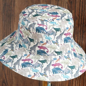 May include: A white bucket hat with a colorful print of various animals, including elephants, giraffes, and birds.