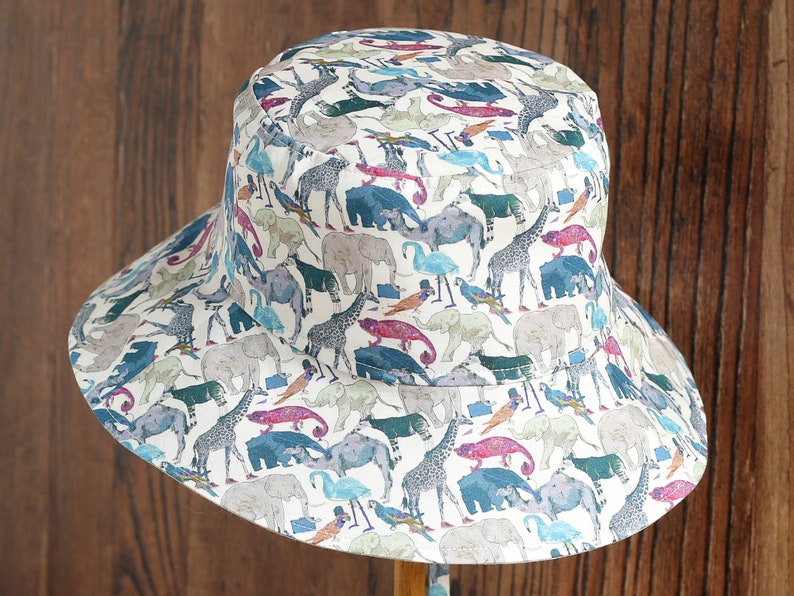 May include: A white bucket hat with a colorful print of various animals, including elephants, giraffes, and birds.