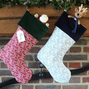 May include: Two Christmas stockings hanging on a brick fireplace mantel. The stocking on the left is red with white polka dots and a green velvet cuff. It has a white tag that says "Remy". The stocking on the right is white with blue polka dots and a navy blue velvet cuff. A stuffed reindeer is peeking out of the top of the stocking.