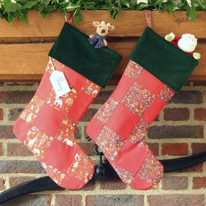 May include: Two festive Christmas stockings, red with patchwork patterns and green velvet tops, hang from a wooden mantel. One has a tag with the name "Barry". A small reindeer and Santa Claus are inside.
