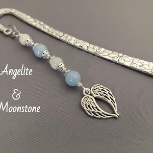 Puede incluir: Marcapáginas plateado con diseño floral y un dije de cuentas. El dije presenta cuentas azules y blancas y un par de alas de ángel. También se ve el texto "Angelite & Moonstone".