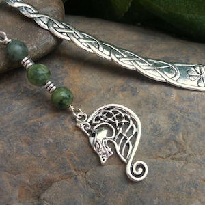 Peut inclure: Signet en argent avec un motif de nœud celtique et un charme en pierre verte. Le charme est un motif de nœud celtique avec une tête de loup au centre.
