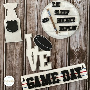 May include: Wooden signs with hockey-themed designs. The signs feature the words "Eat Sleep Hockey Repeat", "Love", "Game Day", and a hockey stick and puck.