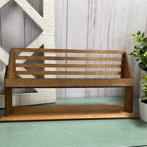 May include: A wooden shelf with a slatted design, perfect for displaying small items. The shelf is made of natural wood and has a rustic look. It is sitting on a light blue surface.