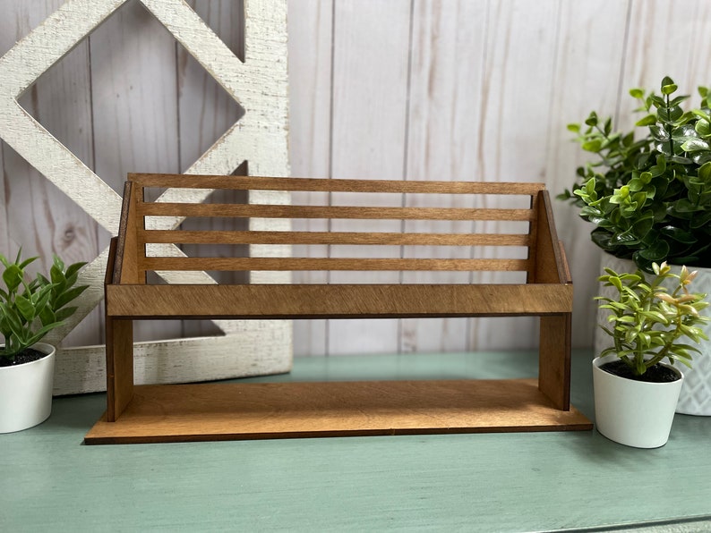 May include: A wooden shelf with a slatted design, perfect for displaying small items. The shelf is made of natural wood and has a rustic look. It is sitting on a light blue surface.