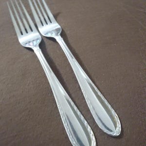 May include: Two silver forks with ornate designs on the handles.
