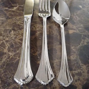 May include: A set of three shiny, silver-colored utensils: a knife, a fork, and a spoon. The knife has a rounded blade, the fork has four tines, and the spoon has a rounded bowl. All three have decorative handles.