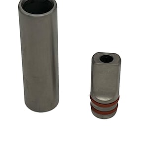 May include: Two silver metal pieces, one a short cylinder and the other a shorter, square-shaped piece with rounded edges. The square piece has two red rubber bands around it.