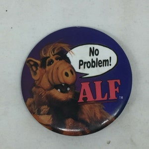 May include: A purple and brown button featuring a cartoon alien with the text "No Problem!" and "ALF" with a trademark symbol.