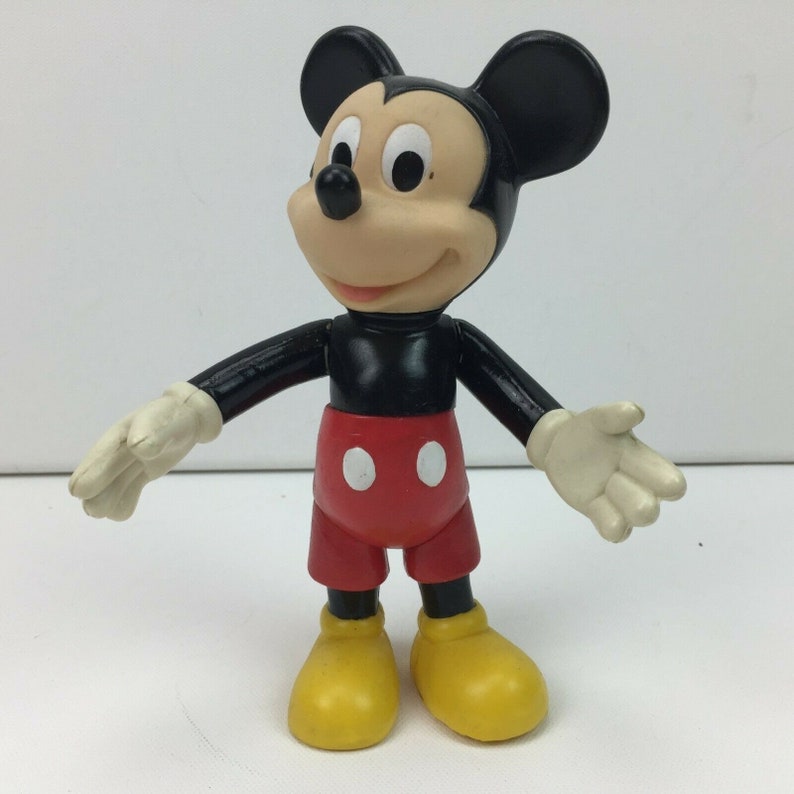 May include: A black and red plastic Mickey Mouse figurine with yellow shoes. The figurine is standing with its arms outstretched.