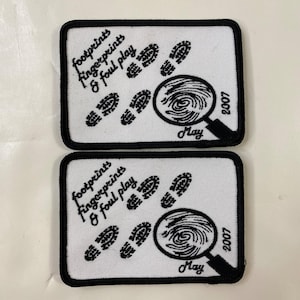 May include: Two rectangular white patches with black borders. Each patch features the text "footprints fingerprints & foul play" and a magnifying glass over a fingerprint. Footprints are also displayed. The date "2007" and the month "May" are included.