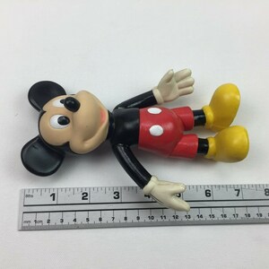 May include: A black and red plastic Mickey Mouse figurine with yellow shoes. The figurine is approximately 10 cm tall.