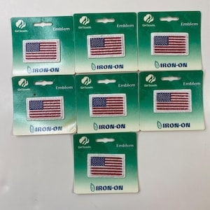 以下が含まれることがあります： アメリカ国旗のアイロン接着ワッペン7枚。各ワッペンは、左上隅に白い星が付いた青い正方形と赤と白のストライプで構成されています。ワッペンは、「Girl Scouts」と「Emblem」の文字が入った緑色の台紙に付いています。