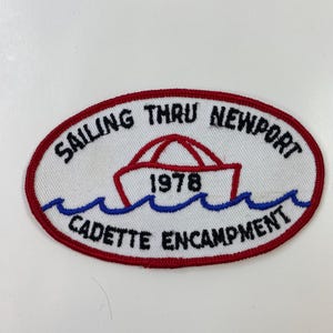 May include: Oval patch with a red border and white background. The patch features the text "SAILING THRU NEWPORT" and "CADETTE ENCAMPMENT" in black. A boat graphic and the year "1978" are in the center, above blue wave graphics.
