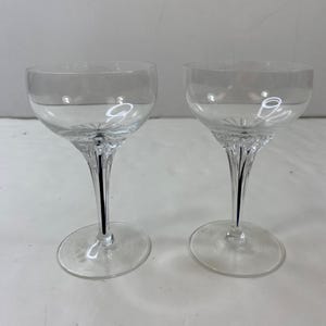 May include: Two clear crystal wine glasses. Each glass features a rounded bowl, a slender, twisted stem, and a circular base. These glasses are designed for serving wine or other beverages. The clear glass allows the contents to be visible.