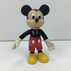 May include: A black and red plastic Mickey Mouse figurine with yellow shoes. The figurine is standing with its arms outstretched.