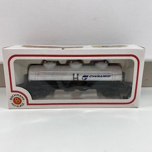 May include: A white model train carriage with black wheels and the words "CYANAMID" printed on the side. The carriage is in a white box with red trim and the words "BACHMANN HO SCALE" printed on the bottom.