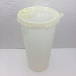 May include: A clear plastic tumbler with a matching lid. The lid has a small, round opening with a cap. The tumbler is cylindrical and appears to be empty. The overall color is a translucent off-white.