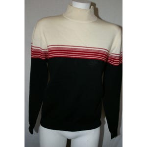 May include: A turtleneck sweater in cream, black, and red. The top portion is cream, with a horizontal band of red stripes. The lower portion and sleeves are black. The sweater is displayed on a mannequin.
