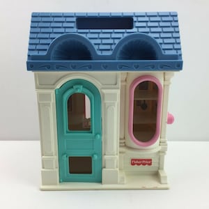 May include: A white plastic toy store with a blue roof, a turquoise door, and a pink window. The store has a Fisher-Price logo on the front.