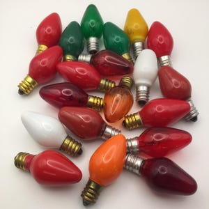 May include: A collection of vintage Christmas light bulbs in various colors, including red, green, yellow, orange, and white. The bulbs have a classic teardrop shape with brass-colored bases. These decorative bulbs are ideal for holiday decorating.