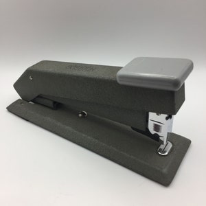 May include: A gray stapler with a light gray top. The stapler has a textured surface and a chrome staple exit. The brand name is embossed on the top of the stapler.