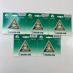 Puede incluir: Cinco parches termoadhesivos Girl Scouts Try-Its. Cada parche es un triángulo con un diseño colorido de amarillo, naranja, morado y verde. Los parches están en tarjetas de respaldo verdes con las palabras "Girl Scouts" y "Try-Its".