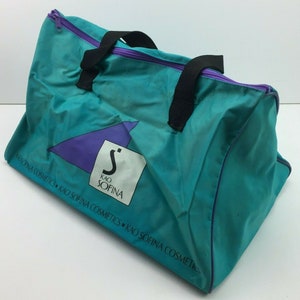 May include: A teal blue travel bag with purple trim and black handles. The bag has a white logo with the text "Kao Sofina" and a purple triangle with a stylized "S" in the center. The text "Sofina Cosmetics Kao Sofina Cosmetics Kao Sofina Cosmetics" is printed around the bottom of the bag.