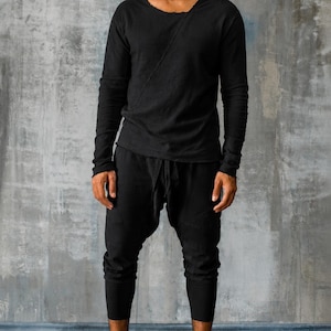 May include: A person wearing a black long-sleeve shirt with a unique neckline and black pants. The outfit is completed with black high-top sneakers. The clothing appears to be made of a soft, flowing material.