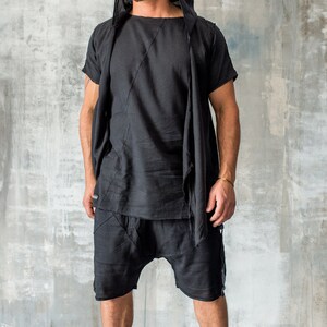 May include: A black hooded top with a long, flowing scarf. The top has a short sleeve and a relaxed fit. The model is wearing black shorts and black trainers.