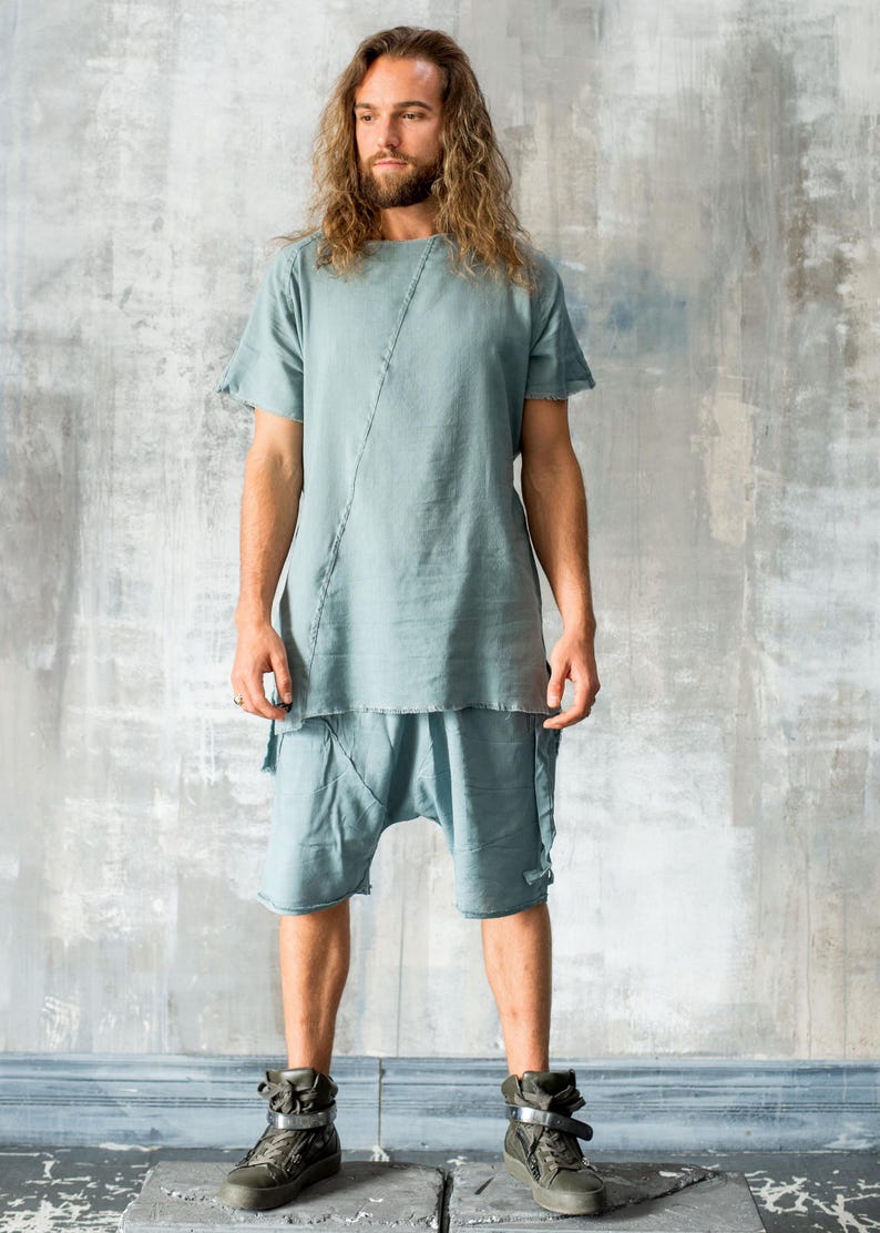 Puede incluir: Conjunto de lino azul claro que consta de una parte superior de manga corta y pantalones cortos a juego. La parte superior tiene una costura diagonal. Los pantalones cortos tienen un ajuste relajado. La persona lleva zapatillas altas verde oscuro.