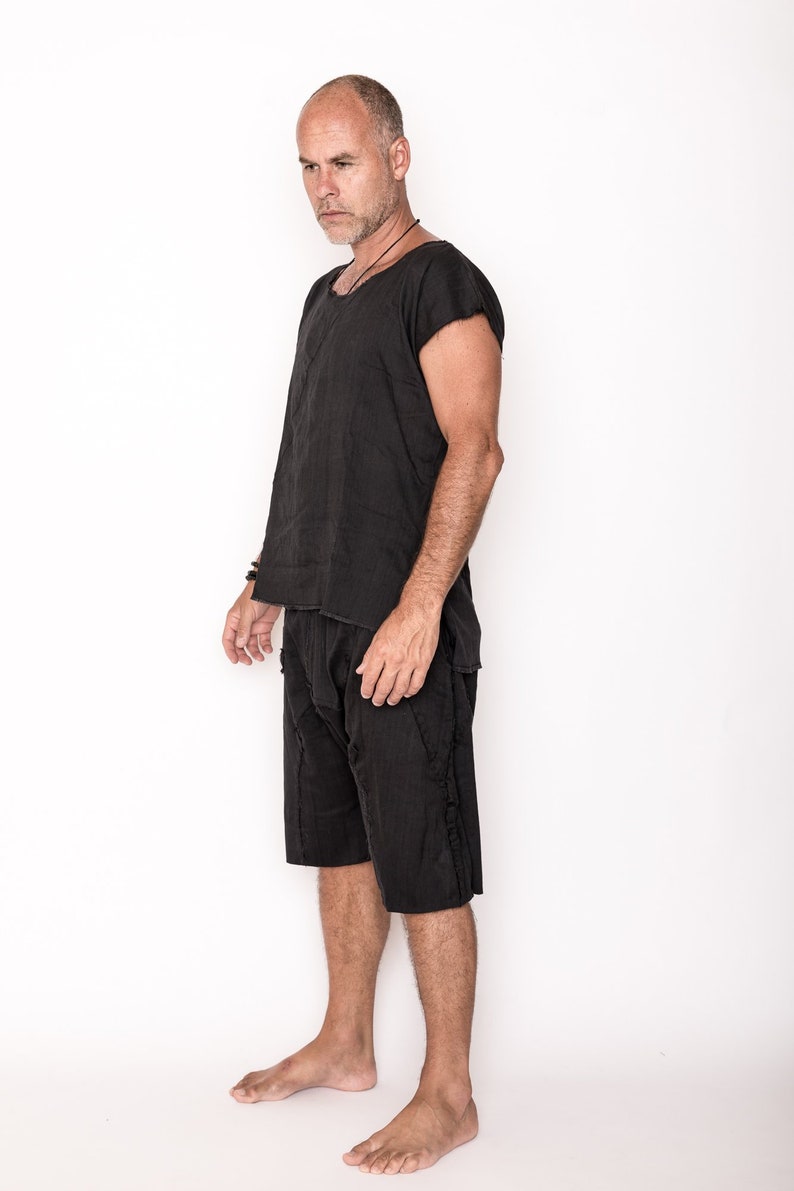 May include: A black linen outfit consisting of a short-sleeved top and matching shorts. The outfit has a relaxed fit and a textured appearance. The model is standing against a white background, showcasing the casual style of the clothing.