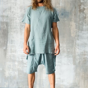 May include: A light blue linen outfit, comprising a short-sleeved top and shorts. The top features a diagonal seam. The shorts have a relaxed fit. The model is wearing olive green high-top trainers. The outfit is casual and stylish.