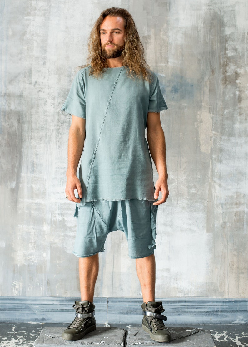 May include: A light blue linen outfit, comprising a short-sleeved top and shorts. The top features a diagonal seam. The shorts have a relaxed fit. The model is wearing olive green high-top trainers. The outfit is casual and stylish.