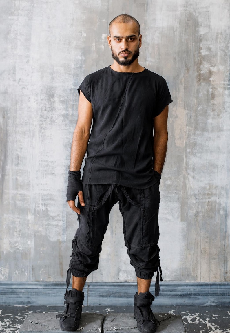 May include: Black outfit consisting of a short-sleeved top and cropped pants. The pants have multiple pockets and straps. The outfit is paired with black high-top sneakers. The person is standing in front of a gray wall.