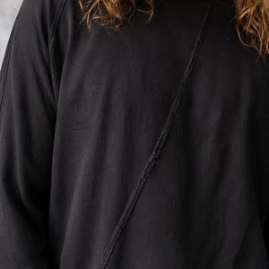 May include: Black long-sleeve shirt with a diagonal seam detail. The shirt has a crew neck and raglan sleeves. The fabric appears to be a soft, textured material. The overall style is casual and relaxed.