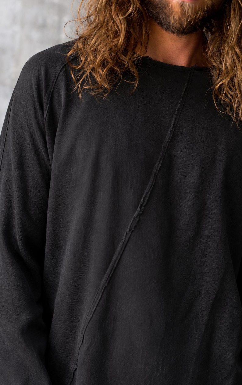 May include: Black long-sleeve shirt with a diagonal seam detail. The shirt has a crew neck and raglan sleeves. The fabric appears to be a soft, textured material. The overall style is casual and relaxed.
