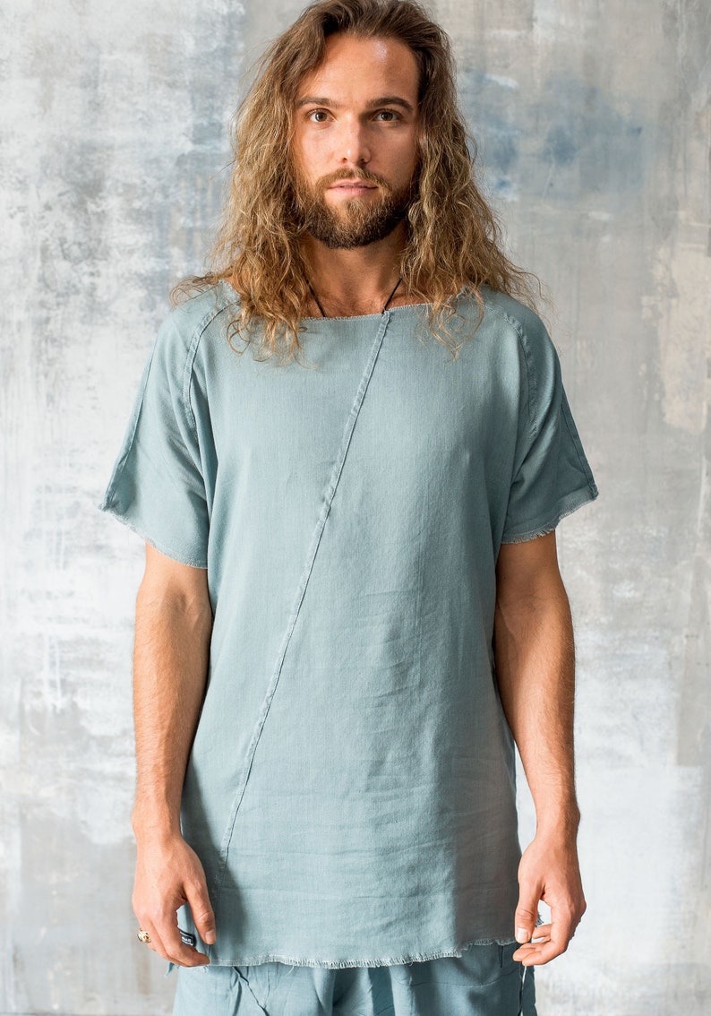 May include: A light blue, short-sleeved shirt with a diagonal seam detail. The shirt has a relaxed fit and a slightly uneven hemline.